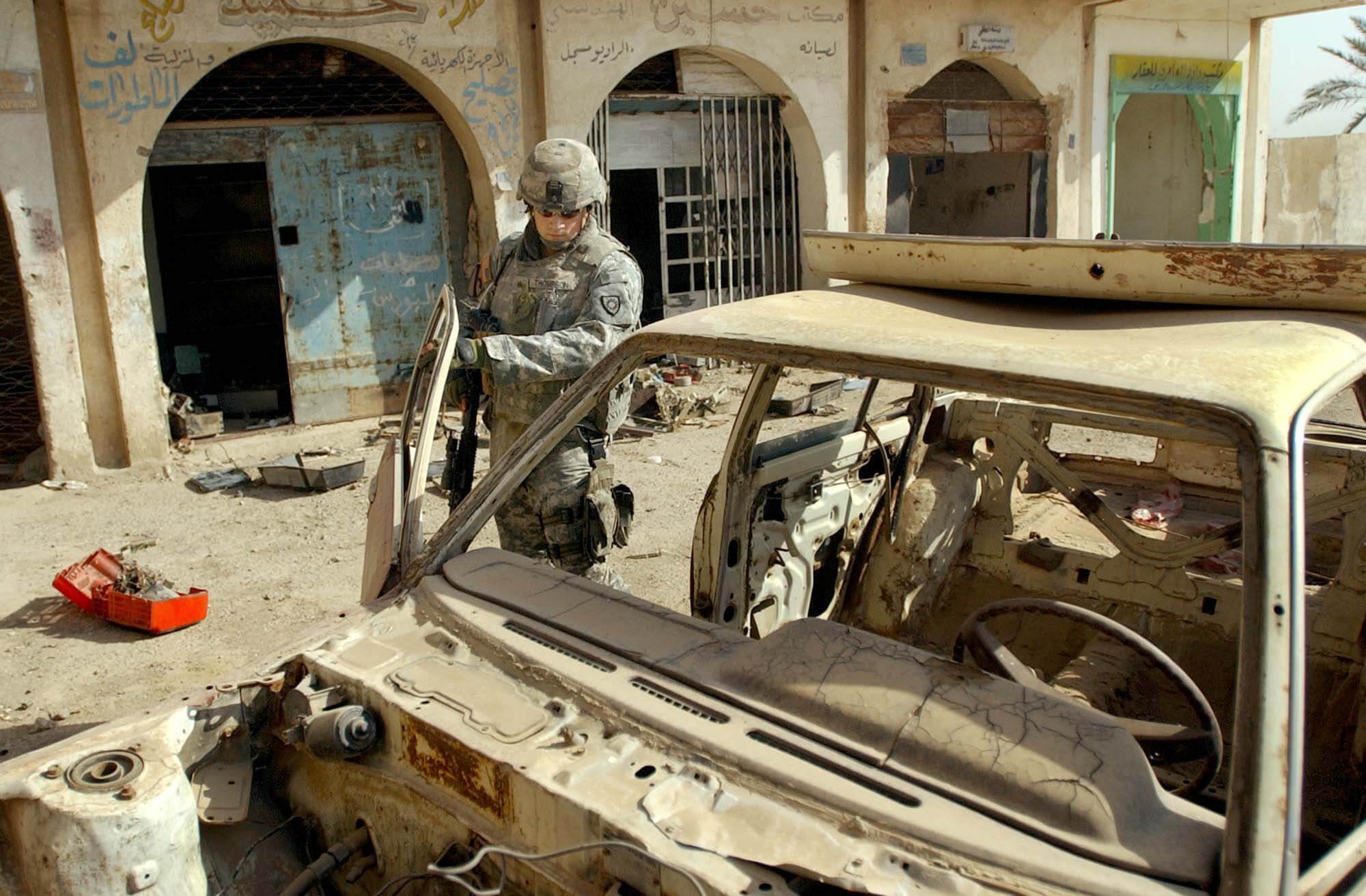 Een Amerikaanse militair bij een verwoeste auto in de Iraakse hoofdstad Baghdad, 2007. Bron: U.S. Army
