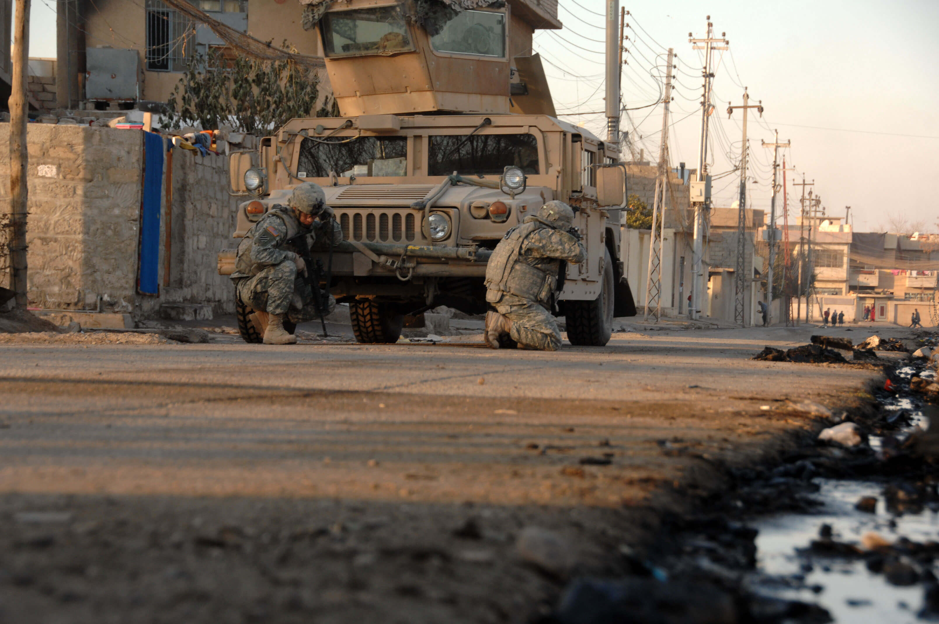Amerikaanse soldaten zoeken dekking achter een voertuig, Irak, 17 januari 2008 © U.S. Army photo by Spc. Kieran Cuddihy